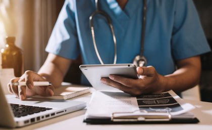 Doctor embracing digital health, working on laptop and iPad 
